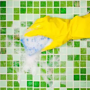 Person wearing rubber gloves scrubbing the tile with a sponge