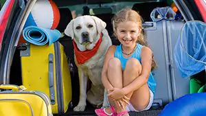 Little girl and a white lab sitting in the trunk of a car