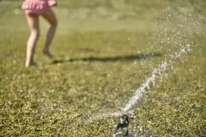 child running in grass through a sprinkler