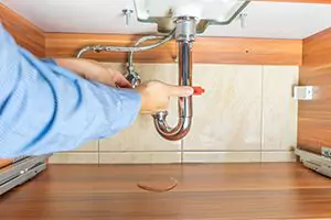 person fixing pipes under a sink