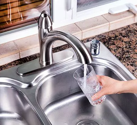 Person filling up cup with water at a kitchen sink