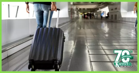 A person carrying a wheeled suitcase along a tiled floor